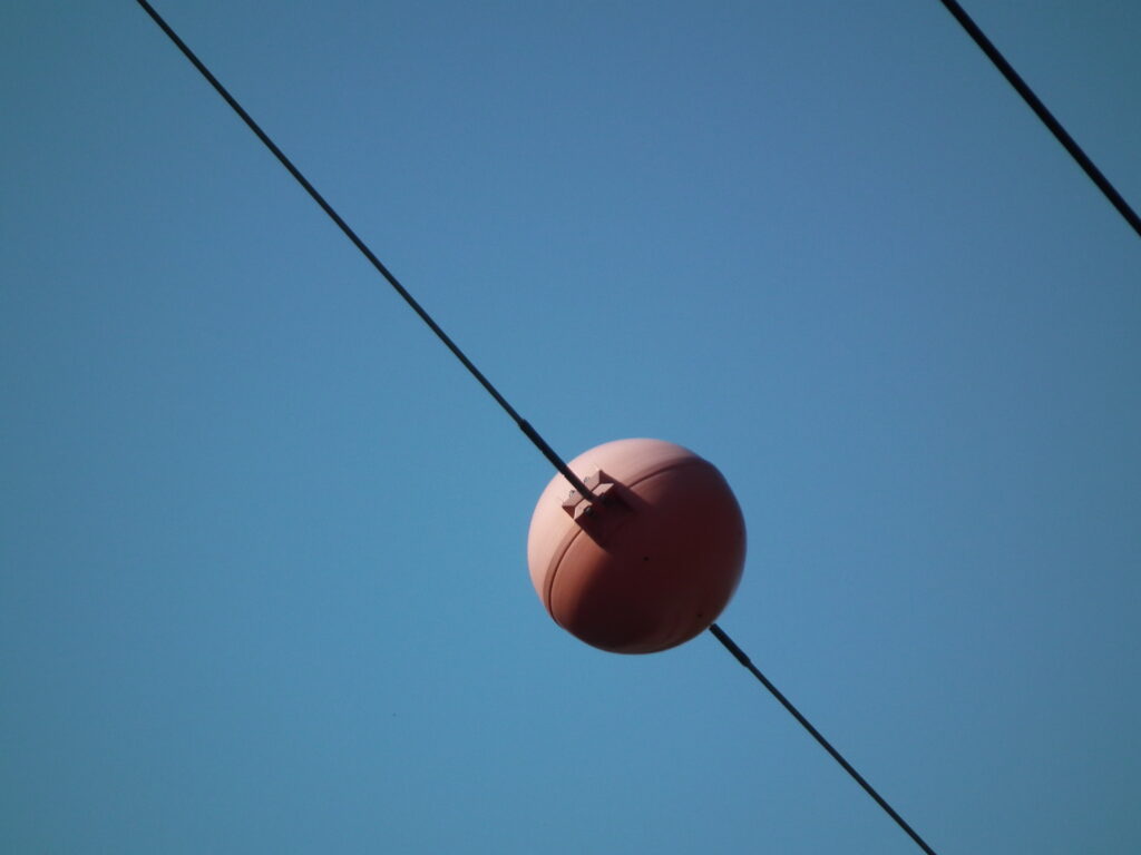 Close-up of a single orange marker ball on a power line wire.